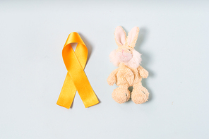 Children's toy rabbit with a Childhood Cancer Awareness Yellow Ribbon on blue background, top view. Childhood Cancer Day February, 15