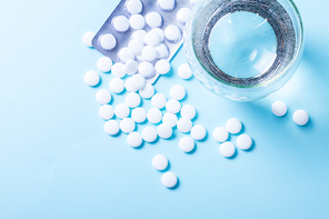 White pills with glass of clear water over blue background with copy space