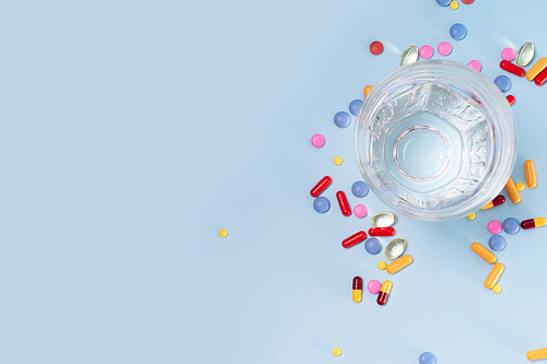 Coloful pills with glass of clear water over plain blue background with copy space. Medical pharmacy concept