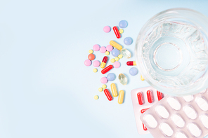 Coloful pills with glass of clear water close up over plain blue background with copy space. Medical pharmacy concept