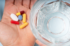 Colorful pills in hand close up with glass of clear water over blue background. Medical pharmacy concept.