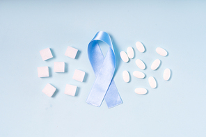 Sugar cubes, Diabetes Awareness Blue Ribbon and pills on plain blue background, flat lay scene. World Diabetes Day concept.