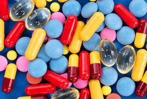 Pile of colorful medical pills on blue background