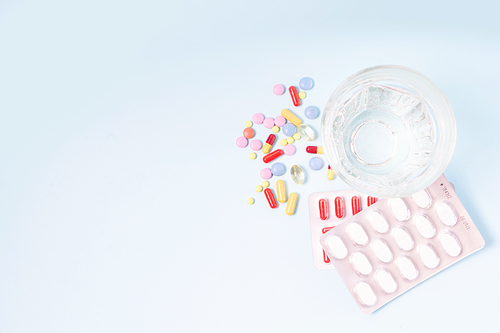 Coloful pills with glass of clear water close up over plain blue background with copy space. Medical pharmacy concept