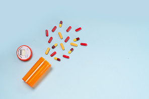 Healthcare concept - orange bottle with scattered pills on blue background with copy space