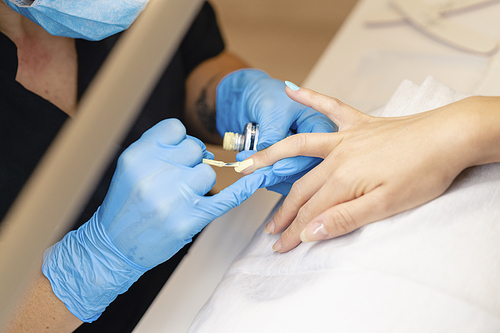 Close-up of Beautician painting her client's nails in blue and yellow nail varnish in a beauty centre