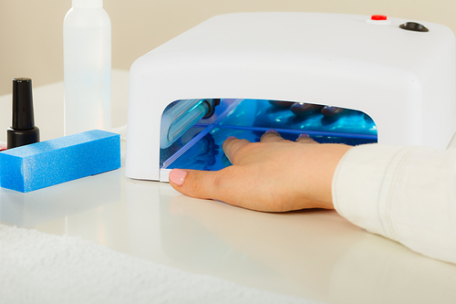 Woman hand in uv led lamp drying gel hybrid manicure on nails. Beauty wellness spa treatment concept.