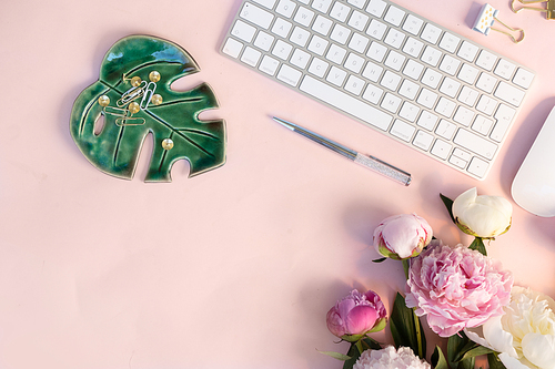Flat lay home office workspace - modern white keyboard with and peony flowers, copy space on pink background