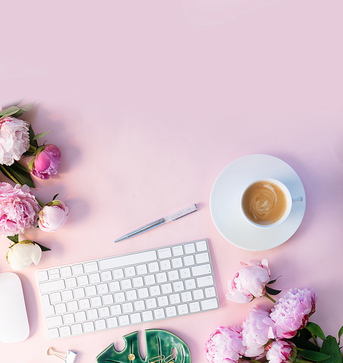 Flat lay home office workspace - modern white keyboard with cup of coffee and peony flowers, copy space on pink desk background