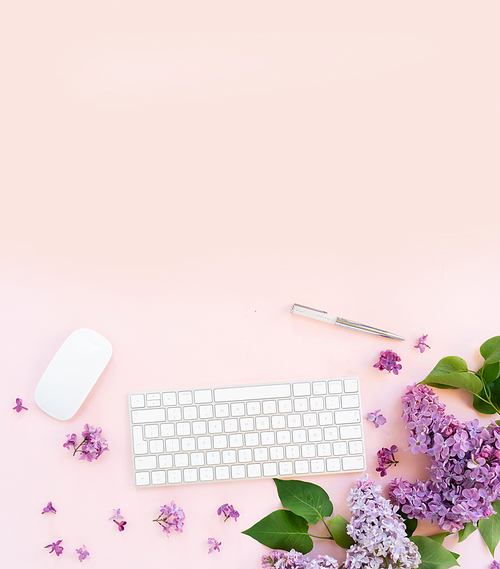 Flat lay top view home office workspace - modern keyboard with lilac flowers, copy space on pink background