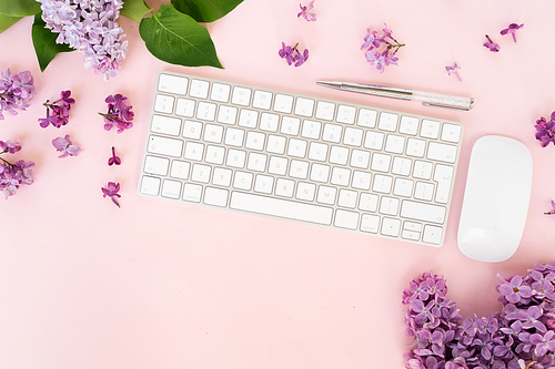 Flat lay top view home office workspace - modern keyboard with lilac flowers on pink desk background