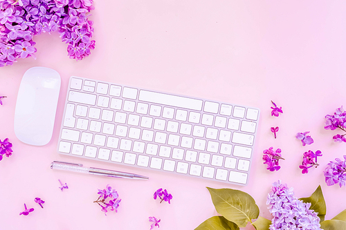 Flat lay top view home office workspace - modern keyboard with lilac flowers on pink desk background, toned