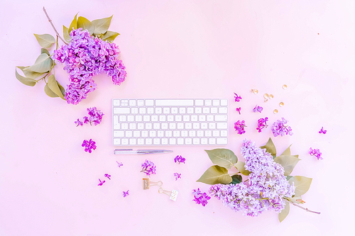 Flat lay home office workspace - modern keyboard with lilac flowers and copy space, toned