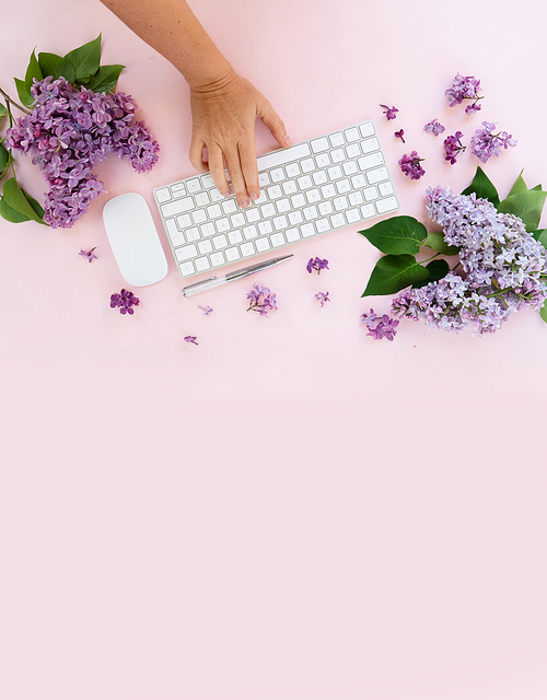 Flat lay home office workspace - modern keyboard with someone hand typing, fresh lilac flowers