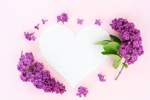Fresh lilac flowers over pink background with copy space on heart paper note, flat lay floral composition