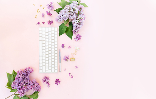 Flat lay home office workspace - modern keyboard with lilac flowers and copy space
