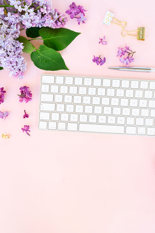 Flat lay top view home office workspace - modern keyboard with lilac flowers and copy space on desk