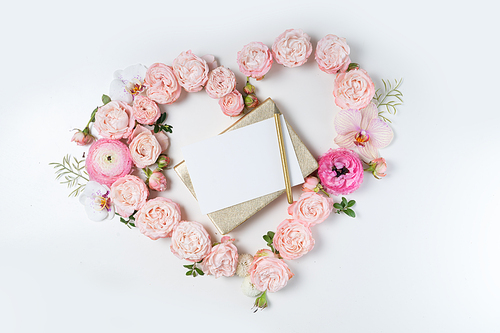 Floral composition. Heart frame made of pink rose and ranunculus flowers on white background. Flat lay, top view, copy space on card