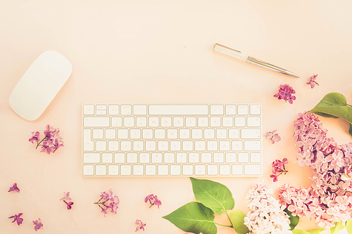 Flat lay top view home office workspace - modern keyboard with lilac flowers on pink background, toned