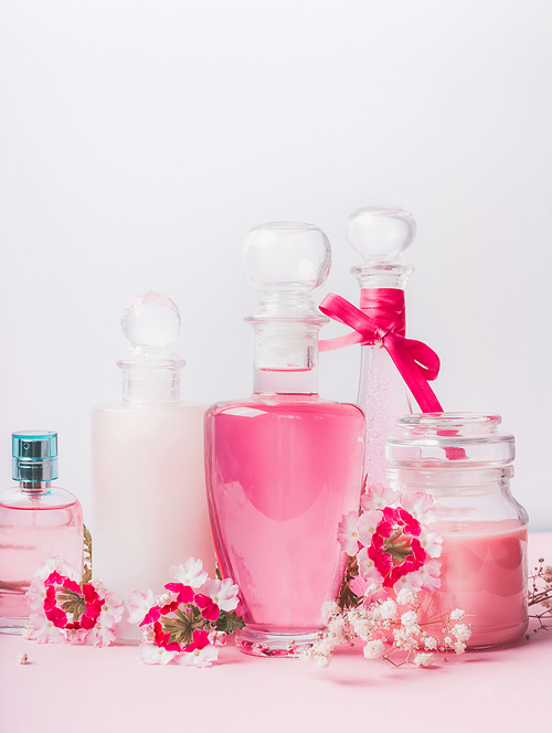 Beauty and skin care concept at light background, front view. Various cosmetic products in bottles and jars with pink  flowers: lotion,perfume, tonic,shampoo