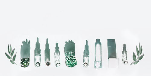 Various modern cosmetic product bottles in sunlight with long shadow and green leaves on white background , top view. Natural cosmetics. Border