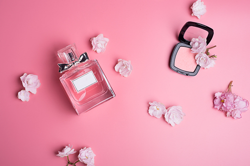perfume bottle  with soft pink blush   around flowers on  pink   background. flat lay