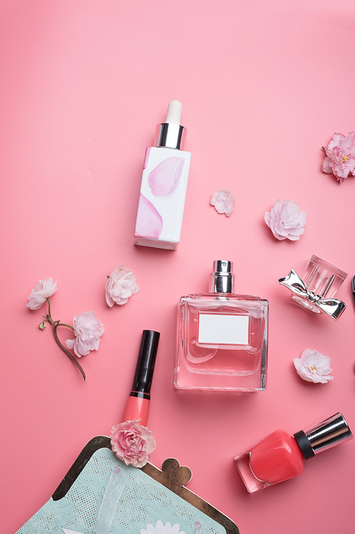 lady set with cosmetics and flowers around pink background. flat lay