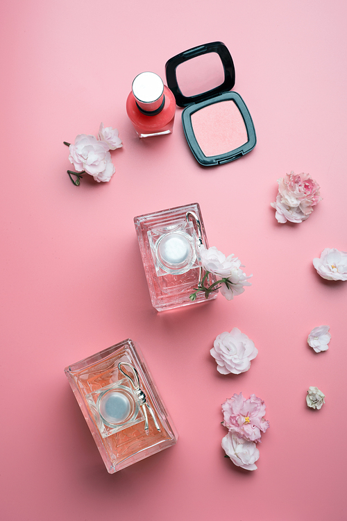 lady set with cosmetics and flowers around pink background. flat lay