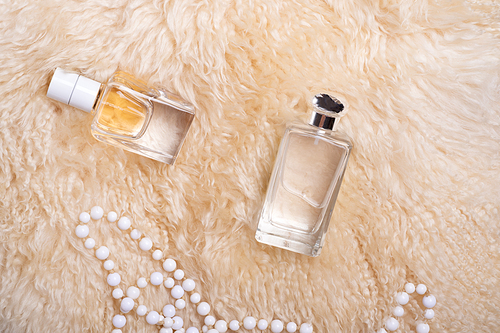 fragrance bottles with necklace at  sheepskin fur.  glamour concept. flat lay