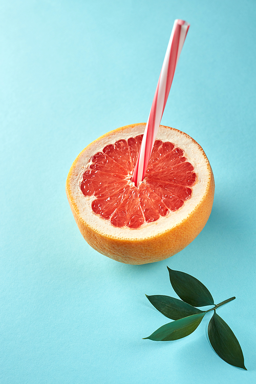 Fresh sliced grapefruit wih straw and green leaves on blue background. Idea creative to produce work within an advertising marketing communications. Business concept