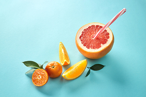 Orange slice, green leaves with straws in grapefruit halves on blue background with copy space. Flat lay