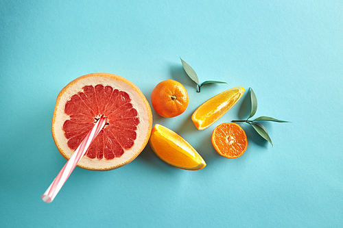 Vitamin drink from half a grapefruit, tangerine and slices of orange on with straws and leaves on a blue paper background top view. Dietic drink