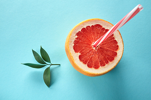 The concept of making natural juices and cocktails from grapefruit. Half a grapefruit on a blue background with a straw and a branch with leaves, top view
