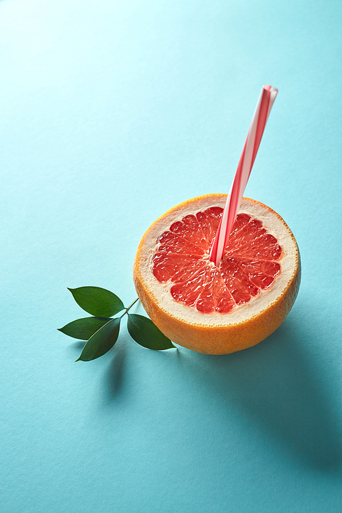 Grapefruit juice. Ripe citrus with straw and green leaves on a blue paper background