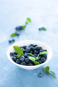 Blueberries with leaves in white bowl on blue background, top view