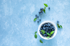 Blueberries with leaves in white bowl on blue background, top view