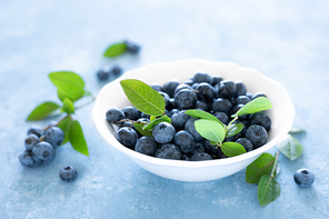 Blueberries with leaves in white bowl on blue background, top view