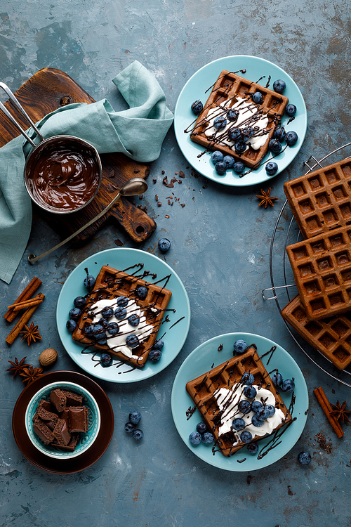 Chocolate belgian waffles with ice cream and fresh blueberry on blue background, top view