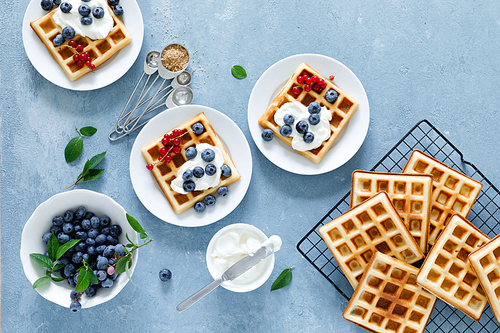 Traditional belgian waffles with cream cheese and fresh blueberry on blue background, top view