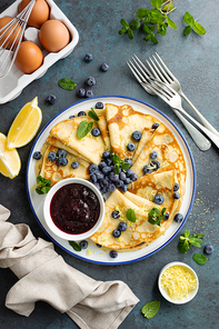 Crepes, thin pancakes with blueberry jam and fresh berries with lemon zest
