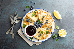 Crepes, thin pancakes with blueberry jam and fresh berries with lemon zest
