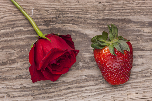 A strawberry and a rose are displayed on an old board.