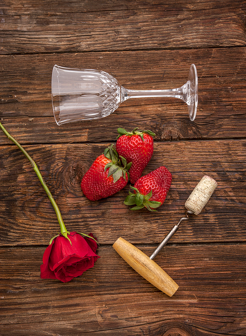 A rose, strawberries, a wine glass, and a cork and corkscrew make up for a romance concept image.