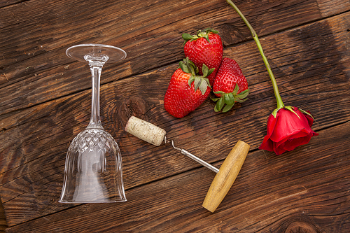 A rose, strawberries, a wine glass, and a cork and corkscrew make up for a romance concept image.