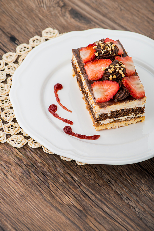 Chocolate strawberry cake on white plate and wooden table.