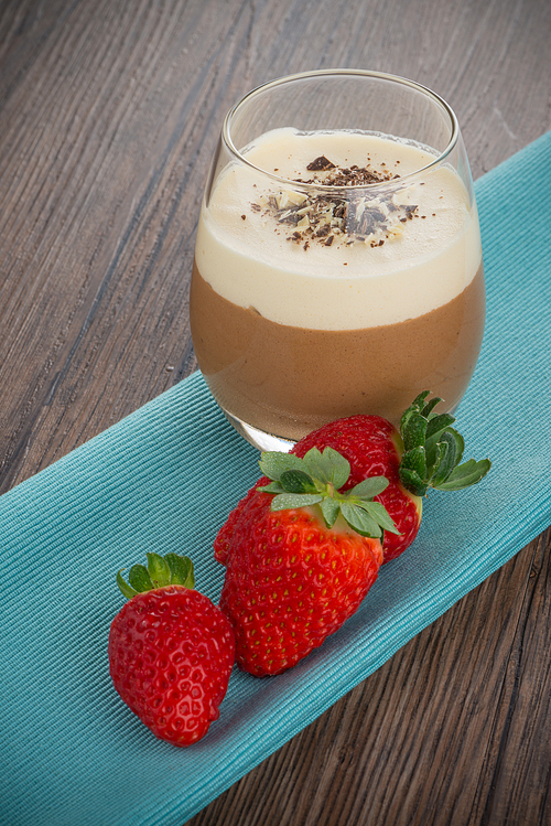 Dessert in glass with chocolate cream and strawberry on wood background