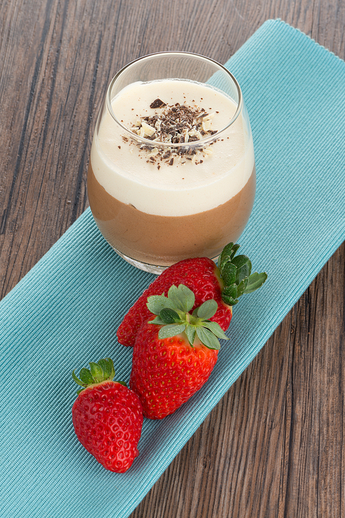 Dessert in glass with chocolate cream and strawberry on wood background