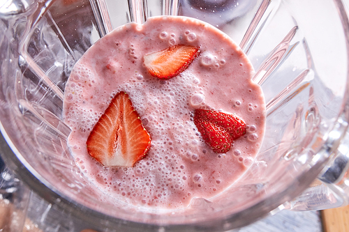 Homemade healthy smoothie dessert with strawberry pieces in a blender bowl. Top view