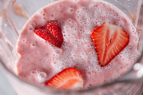 Closeup of milk drink with healthy strawberry slices in a blender. Home-made berry shake. Top view