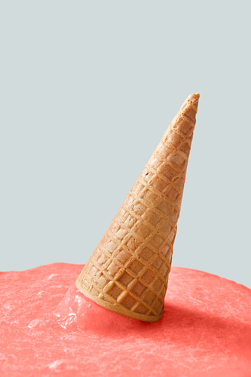 Meltdown of ice cream in a color of the year 2019 Living Coral pantone on a gray background. Falling crispy waffle cone of ice cream. Place for text.
